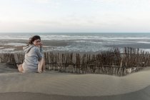 Вид азиатской довольной женщины в отпуске, отдыхающей на песчаном холме и смотрящей в камеру через плечо на Тайване — стоковое фото