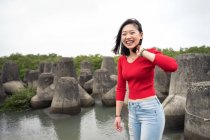 Overjoyed Asian resting woman in casual wear laughing while walking around rocked pond with sky on background — стокове фото