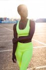 Serious focused African American woman in vibrant yellow sportswear looking away and contemplating in sunbeams alone on street against urban environment — Stock Photo