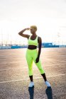 Ernsthaft fokussierte afrikanisch-amerikanische Frau in leuchtend gelber Sportbekleidung, die wegschaut und in Sonnenstrahlen allein auf der Straße gegen die städtische Umwelt betrachtet — Stockfoto