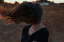 Невизначена жінка з обличчям, покритим довгим волоссям, підірваним сильним вітром, стоячи на лузі в природі — стокове фото