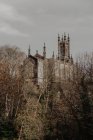 Fachada Shabby de casa antiga com torres e tubos de escape contra o céu nublado em arbustos da cidade — Fotografia de Stock