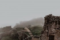 Destroyed old stone castle with fog with walls and stairs with tower on cloudy daytime — Stock Photo