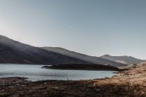 Paysage pittoresque de montagnes avec rochers et lac contre ciel bleu clair au lever du soleil — Photo de stock