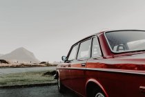 Vista lateral del automóvil rojo antiguo en la carretera que pasa a través de las montañas en el día nublado - foto de stock