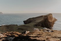Прибрежные скалы и маяк Нейст-Пойнт возле моря против ясного голубого неба в солнечное время дня, остров Скай в Шотландии — стоковое фото