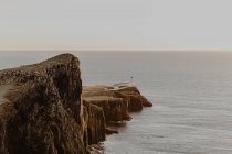Прибрежные скалы и маяк Нейст-Пойнт рядом с морем против ясного голубого неба в солнечное время дня на острове Скай, Шотландия — стоковое фото