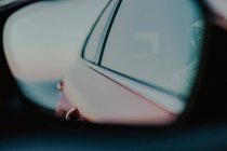 Automóvil rojo reflejado en el espejo retrovisor durante la conducción en carretera en el día soleado - foto de stock