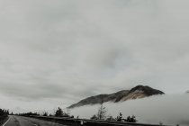 Einsame Gipfel umgeben von Wolken unter grauem Himmel bei nebligem Tag — Stockfoto