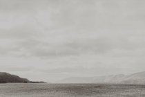 Agua ondulada vacía lavando la costa oscura rodeada de montañas bajo un cielo gris nublado - foto de stock