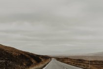Asphalt marked road riding between brown dry hills of valley under gray sky — Stock Photo