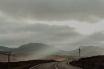 Asfalto marcato strada equitazione tra marrone colline asciutte della valle sotto cielo grigio — Foto stock