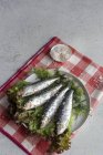 Сверху приготовленная соленая скумбрия подается на листьях салата с кусочками морской соли на тарелке на белом фоне — стоковое фото
