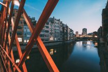 Picturesque city scenery of apartment buildings located on canal behind red bridge railing in early evening, Girona, Spain — Stock Photo