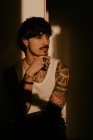 Young man with mustache and tattoos in white tank top standing with hand on chin — Stock Photo