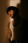 Joven hombre guapo con bigote y tatuajes apoyados en la pared en la sombra - foto de stock