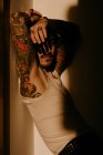 Giovane bell'uomo con baffi e tatuaggi appoggiato al muro in ombra — Foto stock