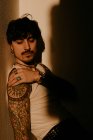 Young handsome man with mustache and tattoos leaning against wall in shadow — Stock Photo