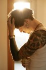 Side view of stylish guy with tattoos leaning against wall with closed eyes — Stock Photo