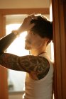Seitenansicht eines jungen stylischen Typen mit Schnurrbart und Tattoos, der sich an die Wand lehnt — Stockfoto