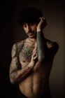 Hombre guapo sin camisa con bigote, piercing y tatuajes posando en el estudio - foto de stock