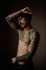 Hombre guapo sin camisa con bigote, piercing y tatuajes posando en el estudio - foto de stock