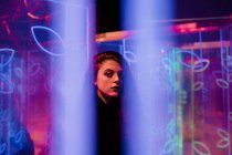 Junge langhaarige Frau in trendiger Kleidung blickt in die Kamera zwischen Leuchtreklamen an der Stadtstraße — Stockfoto