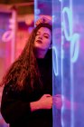 Pretty pensive young woman leaning on wall at city street in neon signs lights — Stock Photo