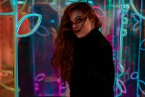Красива меланхолійка з довгим волоссям, що стоїть серед неонових знаків на міській вулиці — стокове фото