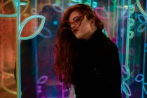 Beautiful melancholic brunette with long hair standing among neon signs at city street — Stock Photo