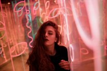 Stylish long-haired woman posing among neon signs at city street — Stock Photo