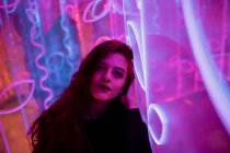 Elegante donna dai capelli lunghi in posa tra i segni al neon in strada città — Foto stock