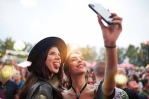 Charmant amis gais en chapeau noir s'amuser grimaçant et prendre selfie sur téléphone mobile dans la journée lumineuse au festival — Photo de stock