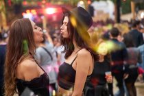 Encantador de cabelos longos amigos elegantes se divertindo olhando um para o outro fazendo gesto de beijo com os lábios em dia brilhante no festival — Fotografia de Stock