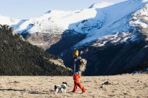 Tourist with backpack and dog walking in valley against snowy mo — Stock Photo