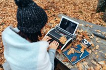Unerkennbare Frau tippt mit Tablet auf Vintage-Schreibmaschine im Herbstlaub auf Steintisch im Eichenwald — Stockfoto
