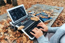 Mani di donna che scrivono su macchina da scrivere vintage con tavoletta in foglie autunnali su tavolo in pietra nel bosco di querce — Foto stock
