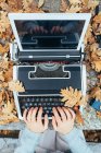 Mãos de mulher digitando na máquina de escrever vintage com tablet em folhas de outono na mesa de pedra na floresta de carvalho — Fotografia de Stock