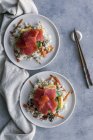 Вид зверху смачного апетитного нарізаного лосося на білому рисі з овочами в тарілках, соєвим соусом і паличками на столі — стокове фото