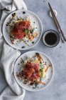 Вид на вкусный аппетитный нарезанный лосось на белом рисе с овощами в тарелках, соевым соусом и палочками на столе — стоковое фото