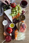 Von oben gesichtslose beschnittene Hände, die Snacks aus einem hölzernen Tablett mit Fleischstücken, Gemüsefrüchten und einem Glas Rotwein essen — Stockfoto
