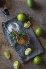 Overhead fresh limes and peppermint leaves placed on napkin and table near rum and brown sugar for mojito preparation — Stock Photo