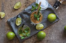 Limette fresche e foglie di menta piperita poste su tovagliolo e tavola vicino al rum e zucchero di canna per la preparazione del mojito — Foto stock