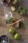 Frische Limetten und Pfefferminzblätter auf Serviette und Tisch in der Nähe von Rum und braunem Zucker zur Mojito-Zubereitung — Stockfoto