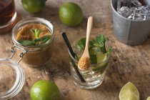 Overhead fresh limes and peppermint leaves placed on napkin and table near rum and brown sugar for mojito preparation — Stock Photo