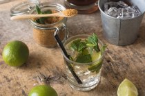 Limette fresche e foglie di menta piperita poste su tovagliolo e tavola vicino al rum e zucchero di canna per la preparazione del mojito — Foto stock