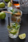 Von oben Glas kalten Mojito aus Rum und Limette mit Pfefferminze und braunem Zucker auf den feuchten Tisch in der Nähe von Eiswürfeln — Stockfoto