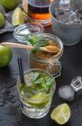 Du dessus verre de mojito froid fait de rhum et de citron vert à la menthe poivrée et à la cassonade et placé sur une table humide près de cubes de glace — Photo de stock