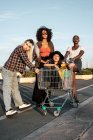 Diversos jovens amigas no casual segurando carrinho de compras vazio para brincadeira em pé e olhando para a câmera — Fotografia de Stock