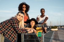 Multiracial group of young women standing around shopping cart on road — Stock Photo
